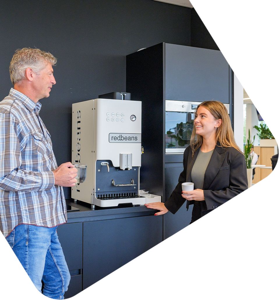 Twee collega’s praten bij een koffieautomaat op een kantoor, e-commerce integratie in bedrijfsomgeving.